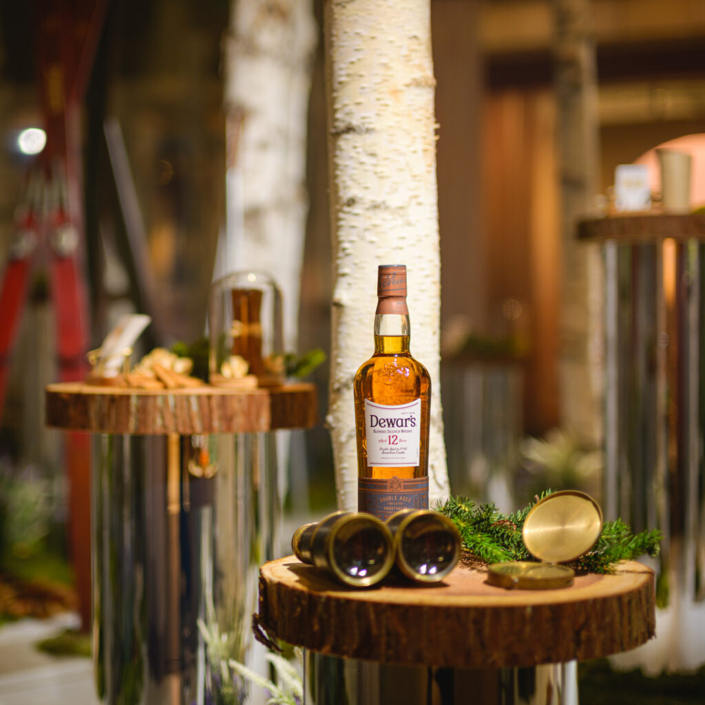 Still life with Dewar’s 12 Year Old whisky bottle set against birch trunks and branded experiential elements from the Dewar’s AMEA activation